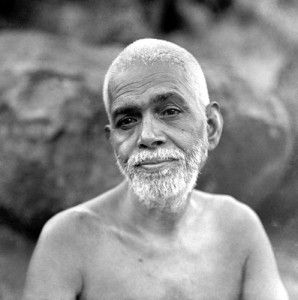 Ramana Maharshi seated bare‑chested among rocks, with a serene and composed expression.